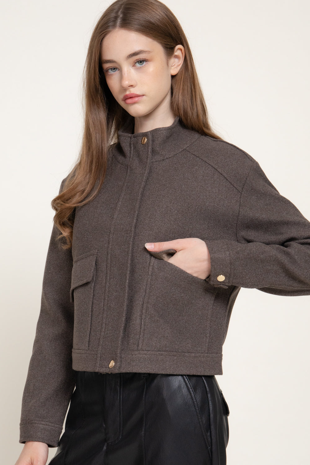 model wearing brown ripped jacket with a stand collar, front snap closure, seam details, and large front pockets.