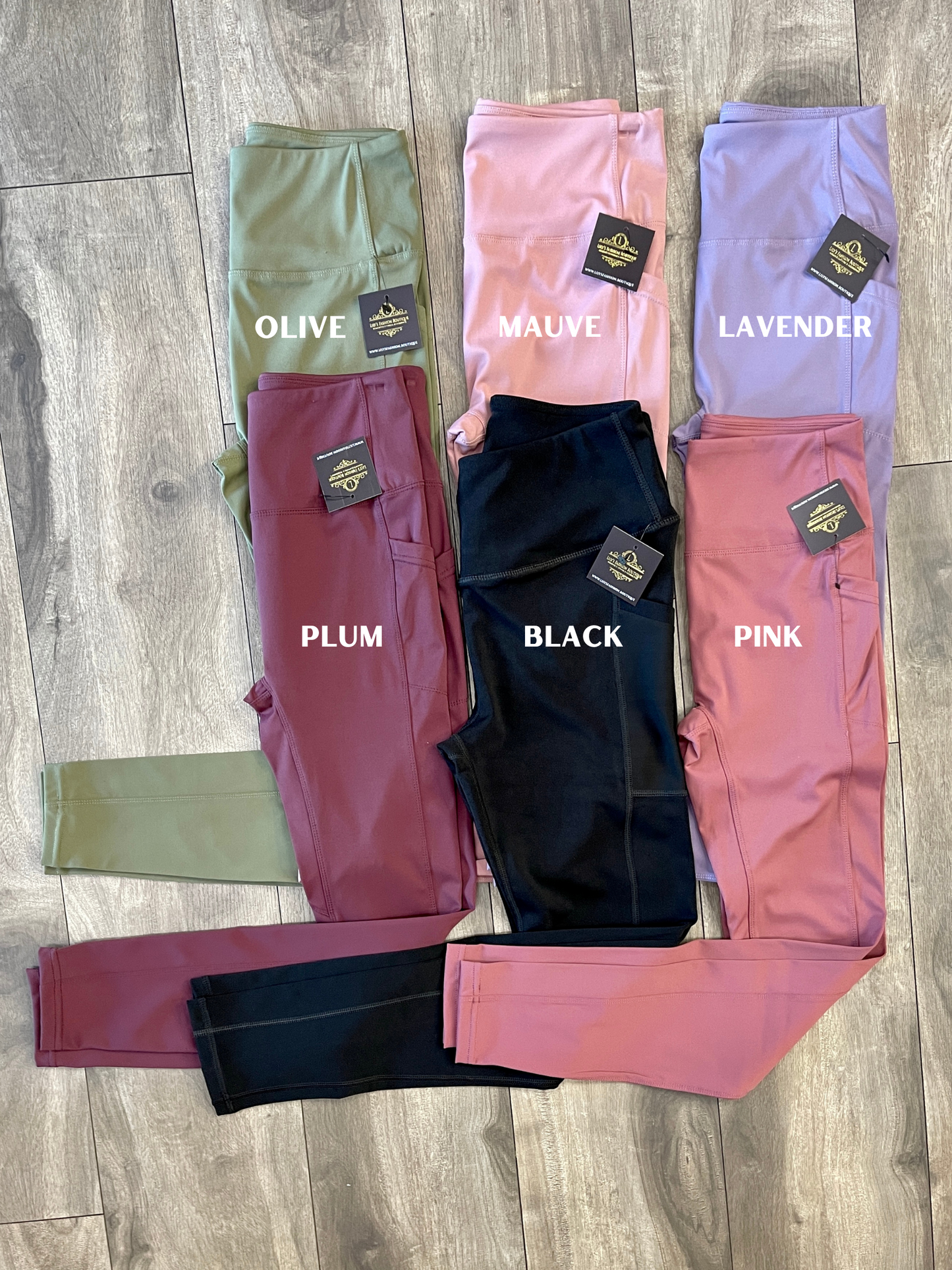 A collection of Grace Yoga Bottoms in various colors, including green, olive, mauve, purple, and pink, laid out flat on a wooden floor.