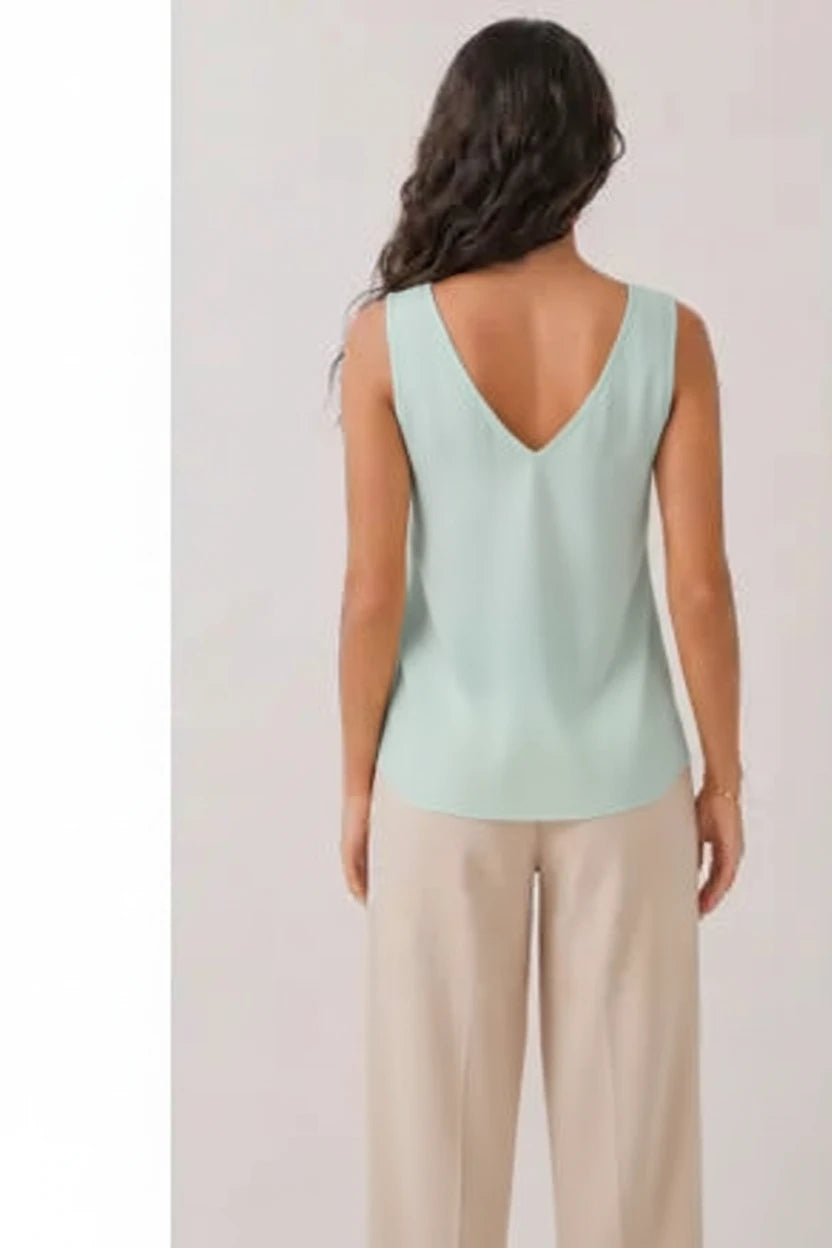 Woman wearing a light green sleeveless top with a V-neckline on a plain background