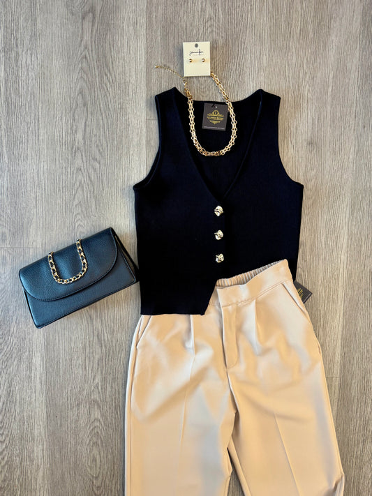 Black button-front vest styled with cream trousers, gold chain necklace, and black handbag outfit flat lay.