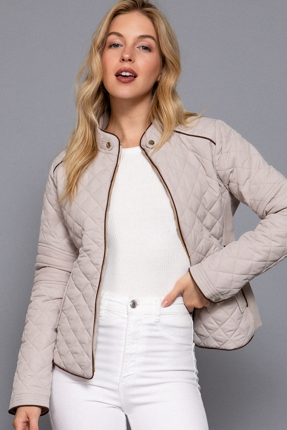 model wearing the Hailey beige quilted jacket with diamond stitching, contrasting trim and front zipper, styled with a white outfit.
