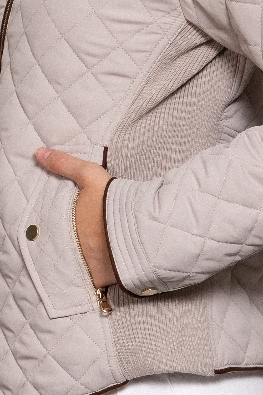 Close-up of the beige quilted jacket showing diamond stitching, suede-look piping and front pocket detail.