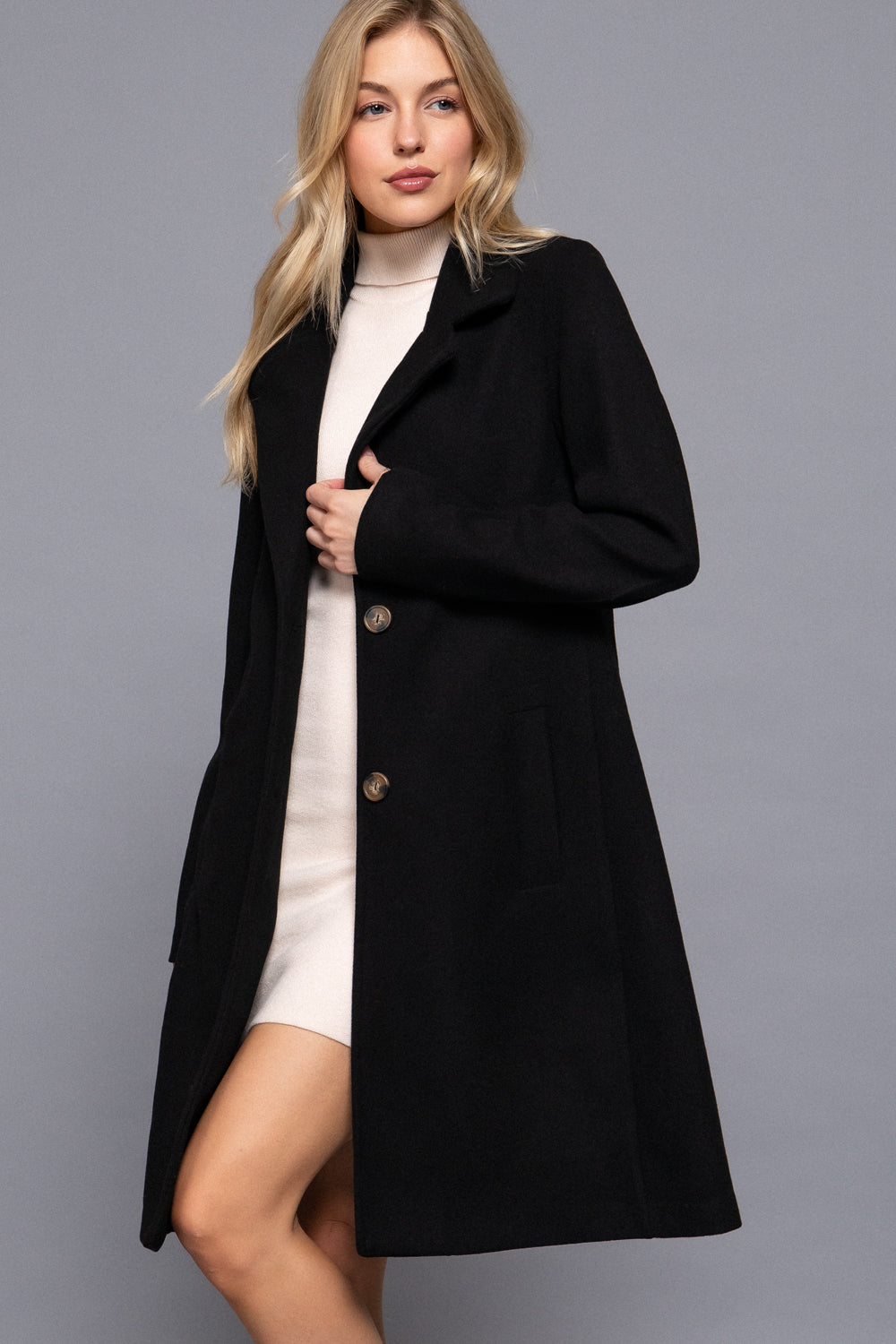 model wearing the Amelia black long-aline coat with classic lapel and button details, styled with a cream mini dress.
