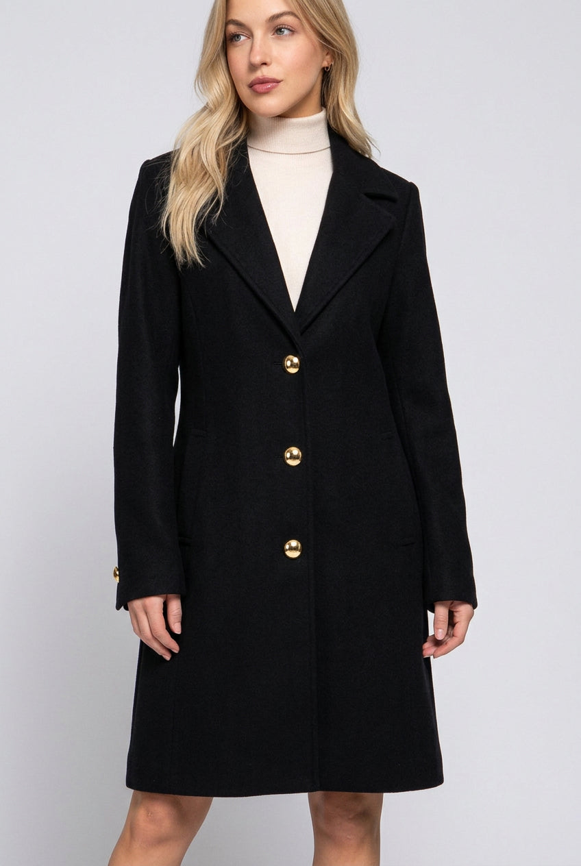 women's black a-line coat with notched lapel collar, button-front closure and pockets, modeled over a cream dress.