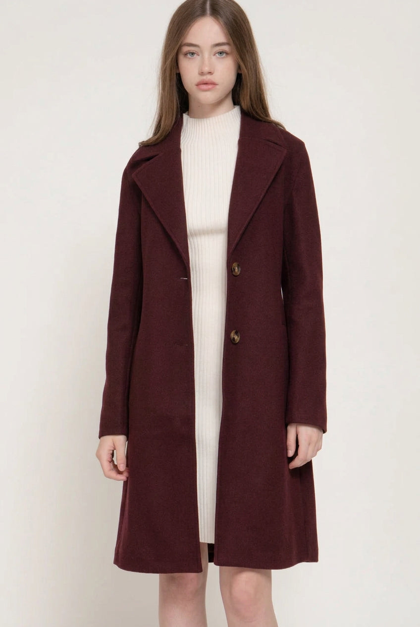 women's burgundy long a-line coat notched lapel collar, button closure and front pockets, styled over a cream outfit.