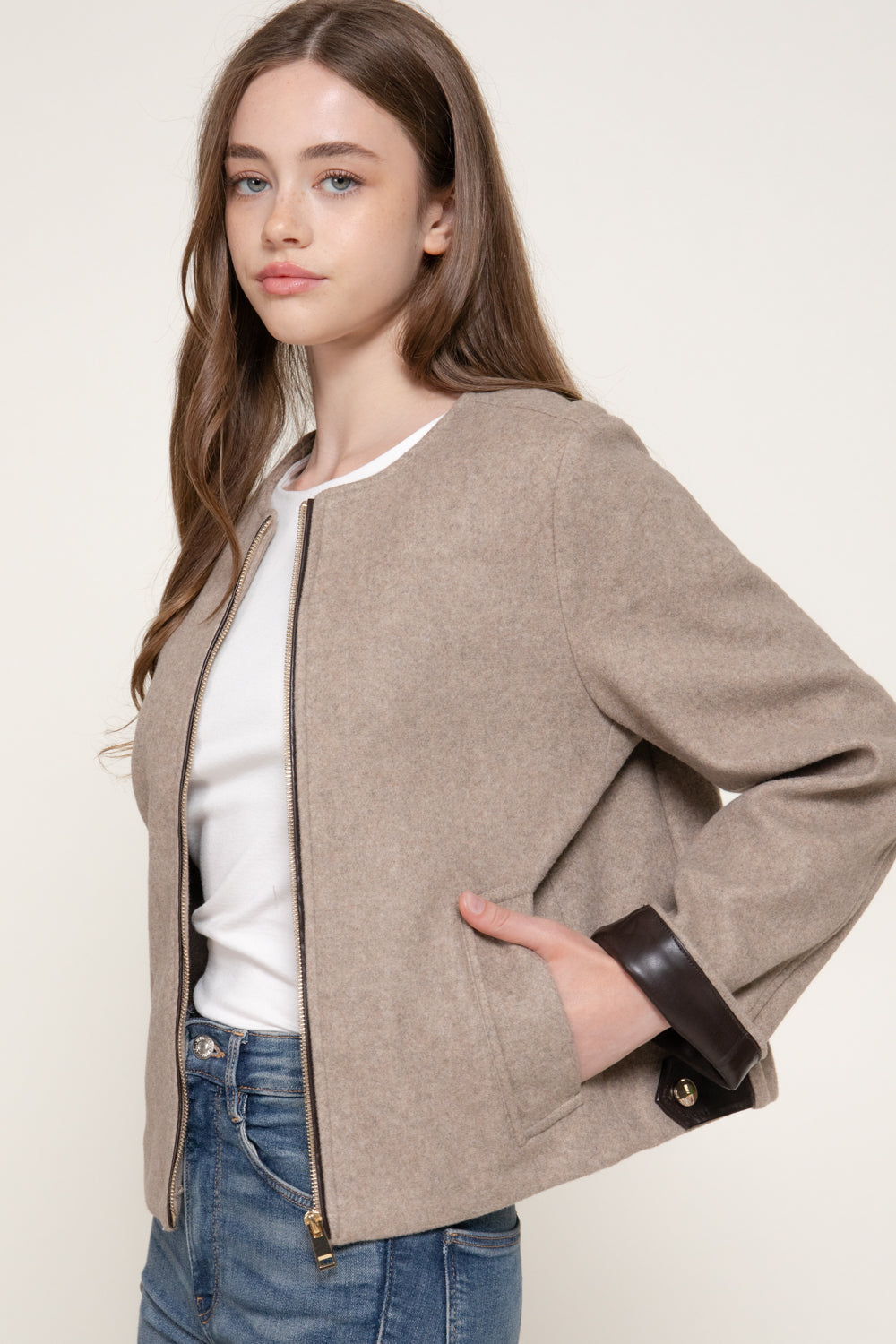 three-quarter view of the beige jacket, showing the front pockets and faux leather cuffs. 