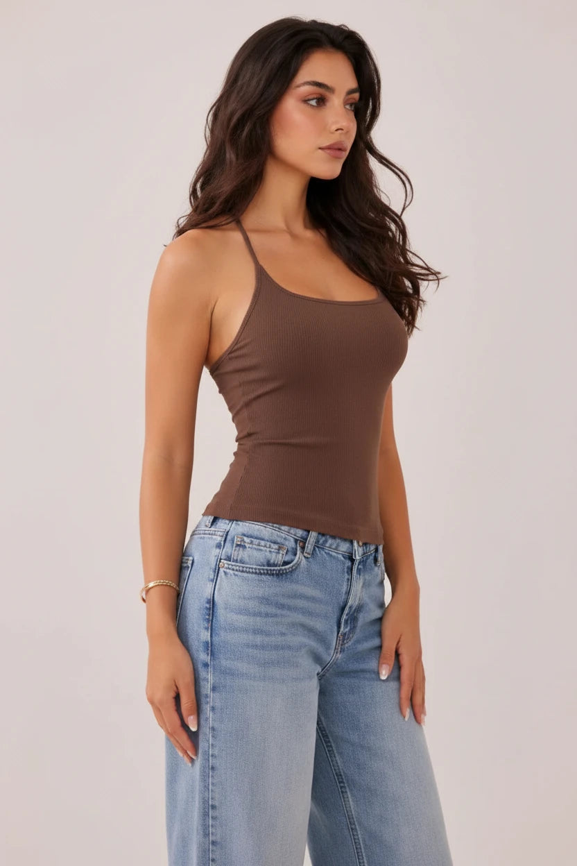 Woman wearing a brown tank top and blue jeans on a light gray background